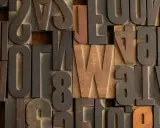 Drewniane czcionki, w tym litery z polskimi znakami, tworzą teksturę przypominającą klasyczny druk. Widać literę "W" w stylu Helvetica.
