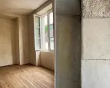 Intérieur d'une pièce aux murs enduits de chaux liège, avec un parquet en bois brut. Gros plan sur la texture rugueuse d'un mur en chaux liège.
