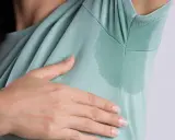 Kobieta z dłonią pod pachą, pokazująca mokre plamy na bluzce. Szukasz domowych sposobów na pocenie się pod pachami?