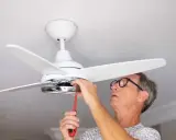 Hombre con gafas ajusta un ventilador de techo pladur con un destornillador.