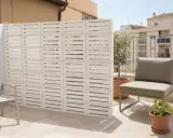 Muros cortina de bloques blancos con diseño de listones horizontales, creando un espacio exterior moderno con silla y plantas.