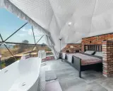 Luksusowy glamping nad jeziorem: wanna z widokiem, łóżko i ceglana ściana w kopułowym wnętrzu.