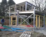 Chantier d'une maison ossature métallique, structure en acier et bois, avec des tuyaux colorés au sol.