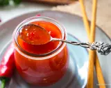 Ein Löffel mit leuchtend roter Thai Chilli Sauce, daneben frische Chilis und Stäbchen.