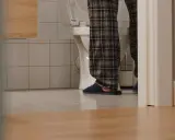 Osoba w piżamie stoi przy toalecie, widać jej nogi i kapcie. Czyżby pojawiły się bąbelki w moczu?