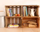 Alte Weinkisten-Ideen: Bücher, Äpfel, eine Kanne und Holzscheite schaffen rustikales Flair.