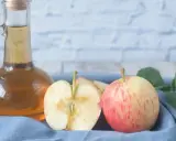 Ein Glas Apfelessig steht neben frischen Äpfeln und Blättern. Perfekt, um essig selber machen.