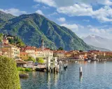 Vista di un paese sul lago d'Iseo, con montagne verdi sullo sfondo. La profondità del lago d'Iseo è suggerita dalla vastità dell'acqua.