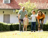 Une famille s'amuse dans le jardin avec un jeu de pétanque en ligne. Les boules colorées sont alignées sur l'herbe.