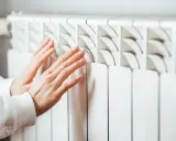Manos cálidas sobre un convector blanco, sintiendo el calor del invierno.