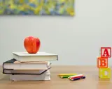 Stos książek z jabłkiem, kredki i kostki z literami A, B, C. Idealny zestaw do nauki, by stworzyć list po angielsku.