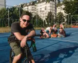 Uśmiechnięty chłopak na rowerze z butelką piwa, obok grupa znajomych. Może to być scena, która zakończy się mandatem za jazdę rowerem po alkoholu.