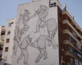 A striking street art style mural depicts a group of bald figures in suits, seemingly engaged in a peculiar, interconnected dance or struggle on a building's facade.
