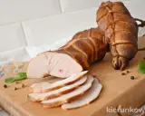 Wędzona pierś z kurczaka, pokrojona w plastry, leży na desce obok całych kawałków, przyprawiona pieprzem i ziołami.
