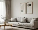 En ljus soffa med kuddar, ett runt träbord med en vas och en golvlampa. Två abstrakta tavlor på väggen bidrar till den minimalistiska inredningen.