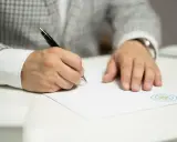 Mężczyzna w eleganckim garniturze podpisuje dokument, który może być wpisem do księgi wieczystej.