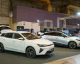 Białe kombi MG5 z otwartą klapą bagażnika i srebrny SUV na wystawie samochodowej.