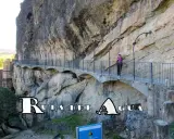 Un pontón de la oliva, parte de la Ruta del Agua, se aferra a un acantilado rocoso. Una mujer camina por el sendero con barandillas.