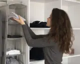 Mujer organiza ropa en un armario con organizador colgante, ideal para saber como organizar un armario sin cajones.