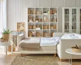Jasny salon z sypialnią na małej powierzchni. Rozkładana sofa, regały z książkami i dekoracje tworzą przytulną przestrzeń.