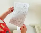 Ręce trzymają dokumenty do zabawy w biuro do druku: "Wielka kapsuła czasu". Zabawne rysunki i miejsce na wpisanie wspomnień.