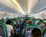 Wnętrze samolotu Transavia, pasażerowie siedzą w rzędach, przygotowani do lotu. Bagaż podręczny schowany w schowkach nad głowami.