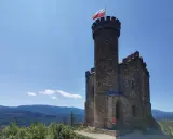 Kamienny zamek henryka na wzgórzu, z polską flagą na wieży, góruje nad zielonymi lasami i błękitnymi górami.