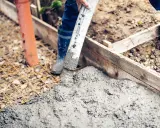 Arbeiter betonieren bei Regen eine Fundamentplatte. Beton fließt aus einem Schlauch auf eine Bewehrung.