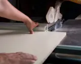 Precyzyjne cięcie płyty meblowej bez odprysków. Ręce stolarza prowadzą płytę do piły tarczowej.