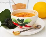 Słodka, karmelizowana crema catalana w ozdobnej miseczce, obok cytryna i jagody.