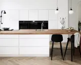 Un plan de travail en bois chaleureux contraste avec les meubles de cuisine blancs. Quelle couleur de plan de travail pour une cuisine blanche ? Le bois est une option parfaite.