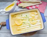 Weißer Spargel in einer Auflaufform mit Zitrone und Kräutern, daneben eine Sauciere mit Sauce.