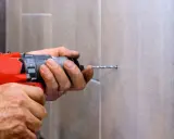 Man usa una broca para azulejo con un taladro para hacer un agujero en una pared de azulejos.