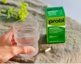 En hand håller ett glas vatten bredvid en ask med Probi Original. Förpackningen förklarar vad innehåller probiotika: levande mjölksyrabakterier.