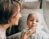 Mama delikatnie wyciera buzię dziecka, które ma żółty katar.