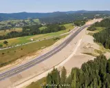 Nowa droga 47 przecina malownicze, zielone wzgórza. Widać ruch samochodów i lasy.