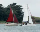 Deux voiliers naviguent sur l'eau, l'un avec une voile rouge, l'autre avec une voile blanche. On dirait un **bateau corsaire** prêt pour l'aventure.