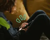 Une personne aux cheveux roux utilise son smartphone, symbolisant quelles peuvent être les principales conséquences de la cyberdépendance : isolement, anxiété, perte de temps.