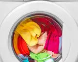 Bunte Wäsche, darunter ein gelber und ein grüner Schwamm, wartet in der Waschmaschine auf das schwamm waschen.