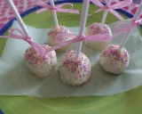 Sju söta cake pops med vit choklad och rosa, gula och lila strössel, dekorerade med rosa band.