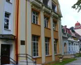 Sanatorium Jan Kazimierz w Dusznikach-Zdroju, z charakterystyczną żółto-kremową fasadą i czerwonym dachem, otoczone zielenią.