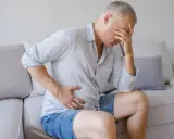Uomo con mano sulla fronte e sull'addome, sofferente. Potrebbe essere un segnale che il deursil fa male al fegato.