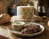 Un steak grillé fumant servi avec une sauce onctueuse à la Fourme d'Ambert, du pain artisanal et un verre de vin rouge.