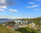 Moderne Seilbahnstation am Monte Baldo mit Panoramablick auf die Berge. Eine Gondel fährt den Hang hinauf.