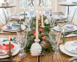 Une table dressée pour les fêtes, avec des assiettes décorées, des bougies allumées et une guirlande de sapin, évoquant la magie des arts de la table.