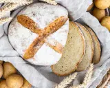 Frisch gebackenes Kartoffelbrot, aufgeschnitten und mit Kartoffeln und Weizenähren dekoriert. Ein tolles Rezept für Kartoffelbrot!