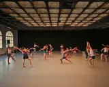 Grupa tancerzy wykonuje dynamiczny gaga taniec w przestronnej sali.
