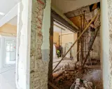 Trwa rozbudowa starego domu. Widać gruz, rusztowania i robotników pracujących nad konstrukcją.