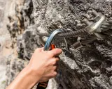 Dłoń zapina karabinek do stalowej liny na via ferrata. Bezpieczeństwo podczas wspinaczki.