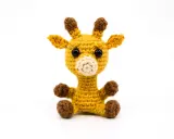 Tierna jirafa amigurumi amarilla, sentada con sus patitas marrones. Sus ojos negros y hocico beige le dan un aspecto adorable.